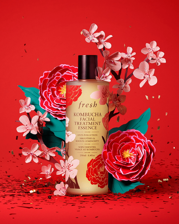 Fresh Kombucha Facial Treatment Essence stands amidst a red backdrop, adorned with paper cherry blossom and camellia flowers.