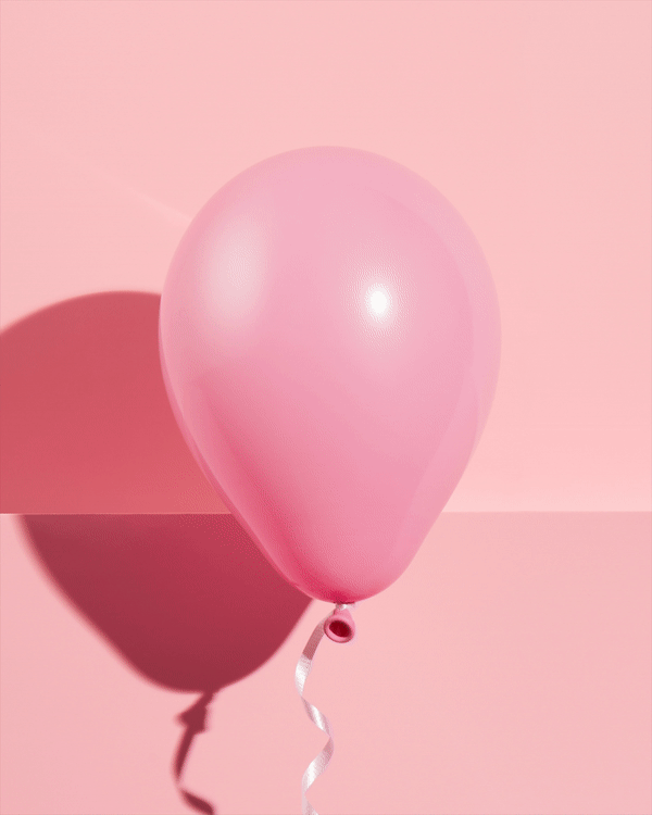 Pink balloon with ribbon on a pink background. A classic party decoration for celebrations and events, casting a soft shadow.