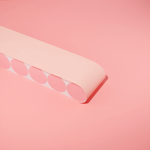 Close-up of a roll of pastel pink round sticker labels on a pastel pink surface, showcasing simplicity and minimalist design.
