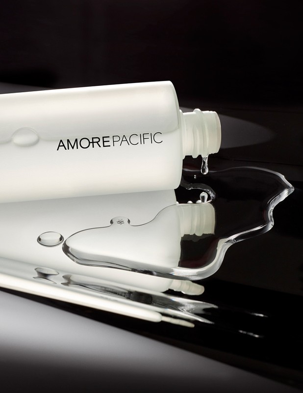 Cosmetic bottle with Amorepacific brand in a studio shot with water drops on a reflective surface, showcasing beauty and product.