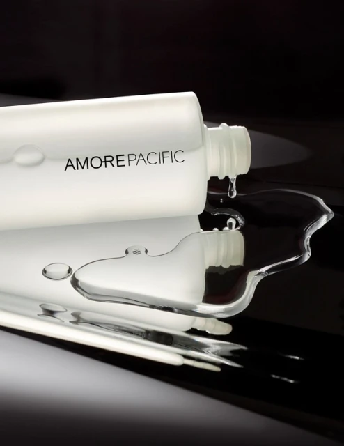 Cosmetic bottle with Amorepacific brand in a studio shot with water drops on a reflective surface, showcasing beauty and product.