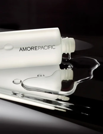 Cosmetic bottle with Amorepacific brand in a studio shot with water drops on a reflective surface, showcasing beauty and product.