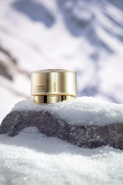 Amore Pacific skincare product is displayed on a snowy rock, with a blurred snowy landscape in the background, showcasing beauty and nature.