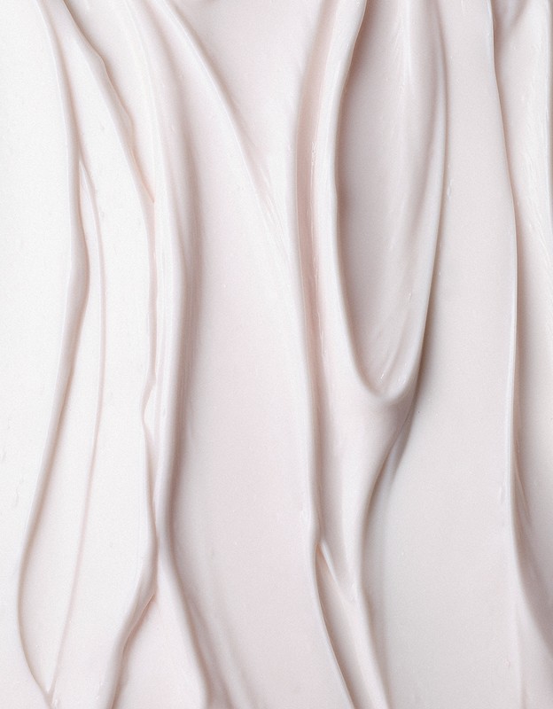 Close-up of rippled, light pink beauty cream filling the frame, showcasing a smooth, soft texture and subtle color variations.