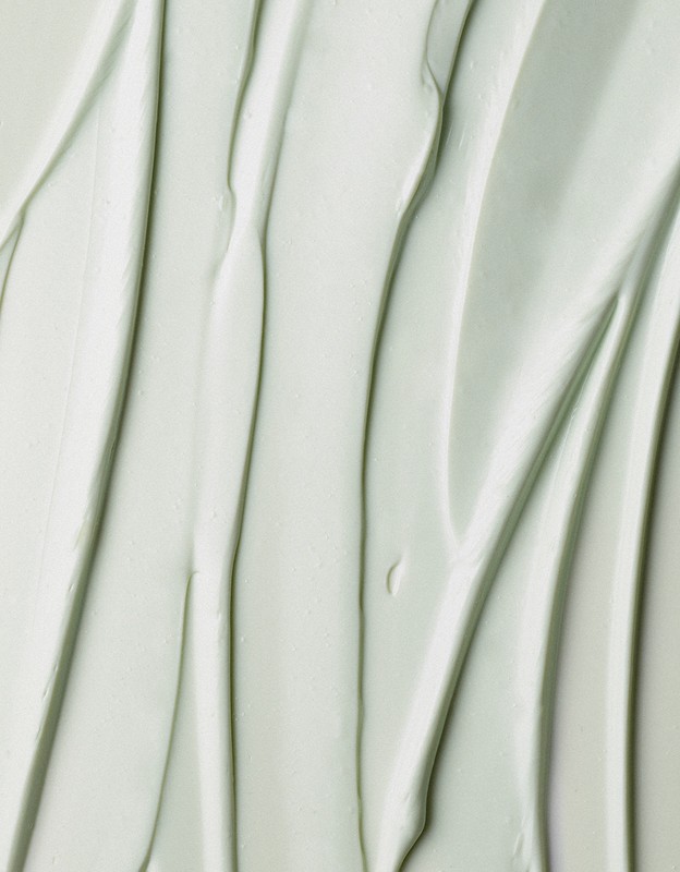 Close-up of smooth, light-green cream with vertical grooves, creating a soothing and textured background for beauty or skincare concepts.
