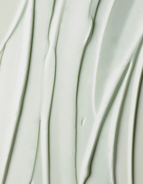 Close-up of smooth, light-green cream with vertical grooves, creating a soothing and textured background for beauty or skincare concepts.