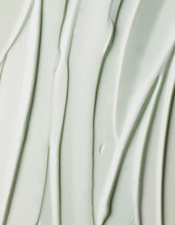 Close-up of smooth, light-green cream with vertical grooves, creating a soothing and textured background for beauty or skincare concepts.