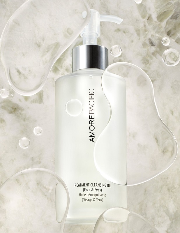 Amorepacific treatment cleansing oil for face and eyes in clear bottle with pump against a marble-like background and clear liquid orbs.