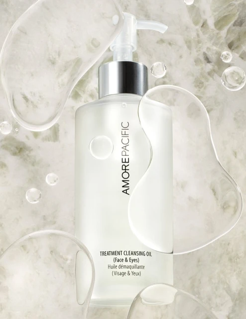 Amorepacific treatment cleansing oil for face and eyes in clear bottle with pump against a marble-like background and clear liquid orbs.