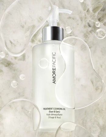 Amorepacific treatment cleansing oil for face and eyes in clear bottle with pump against a marble-like background and clear liquid orbs.