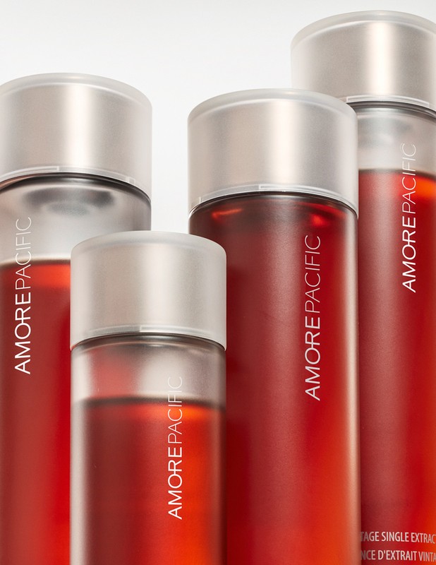 Several red-tinted AmorePacific skincare bottles with silver tops stand against a stark white backdrop in a product shot.