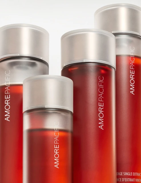 Several red-tinted AmorePacific skincare bottles with silver tops stand against a stark white backdrop in a product shot. 