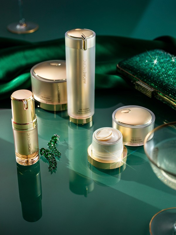Assortment of Amorepacific skincare products in gold and white packaging on a glossy green surface with luxurious accessories.