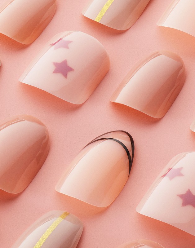 Close-up view of light pink artificial nails with designs including black lines, yellow stripes, and purple stars against a pink backdrop.