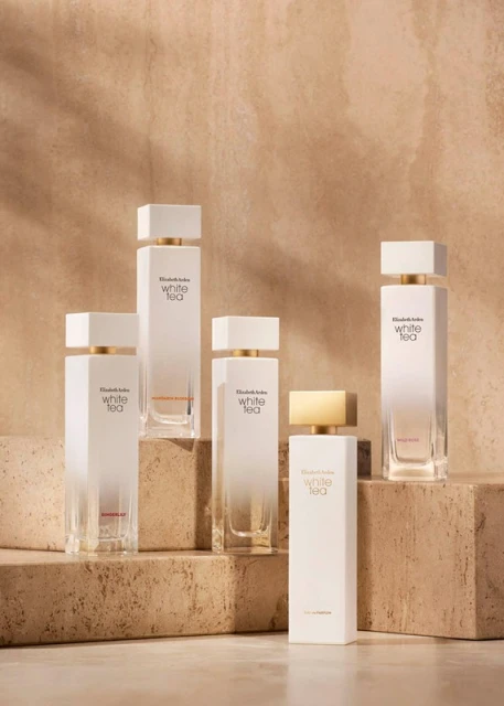 Several bottles of Elizabeth Arden White Tea perfume are arranged on a tiered stone surface, showcasing their clean and elegant design.