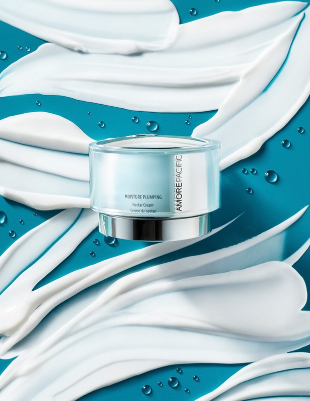 Moisturizing cream in a clear jar with silver accents, showcased against a bright turquoise background with white cream swirls.