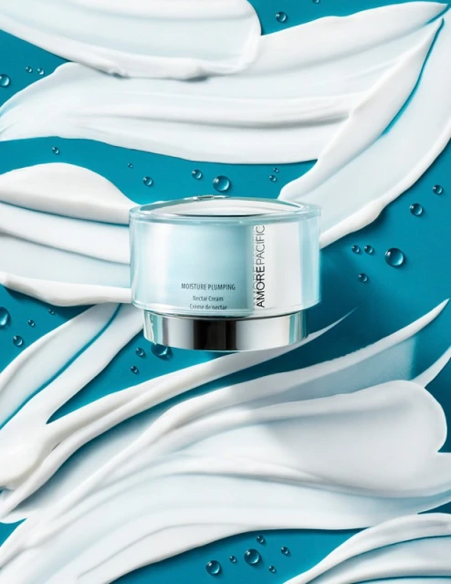 Moisturizing cream in a clear jar with silver accents, showcased against a bright turquoise background with white cream swirls.