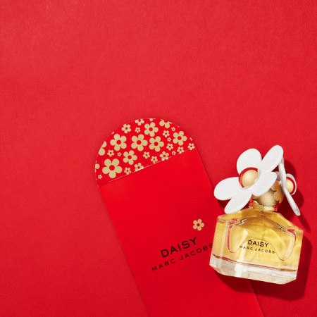 Marc Jacobs Daisy perfume bottle with red envelope featuring flower pattern, against a red background, promoting fragrance.