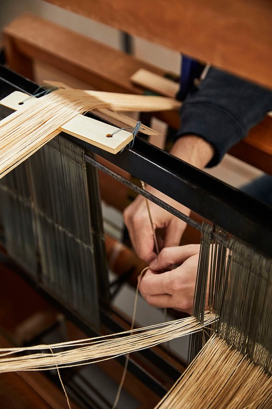 Close-up of hands weaving light brown threads on a loom, showcasing the textile creation process in a crafting environment.