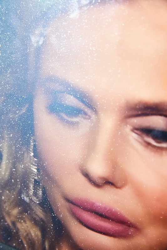 Close-up portrait of a woman with pink lipstick and sparkling earrings under a heavily textured, glittering surface.