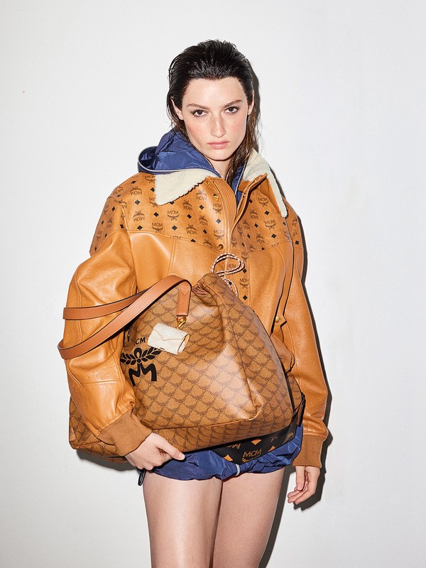 Portrait of a woman wearing a brown printed jacket and shorts, holding a matching handbag in a studio setting with white background.