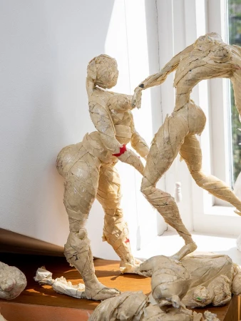 Figurative art sculpture featuring two nude figures in a dynamic pose, crafted with textured material against a bright white background.
