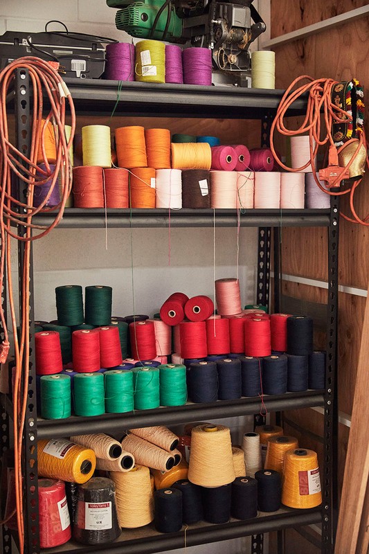 Organized shelving unit filled with vibrant spools of yarn in various colors. Crafting and sewing materials displayed indoors.