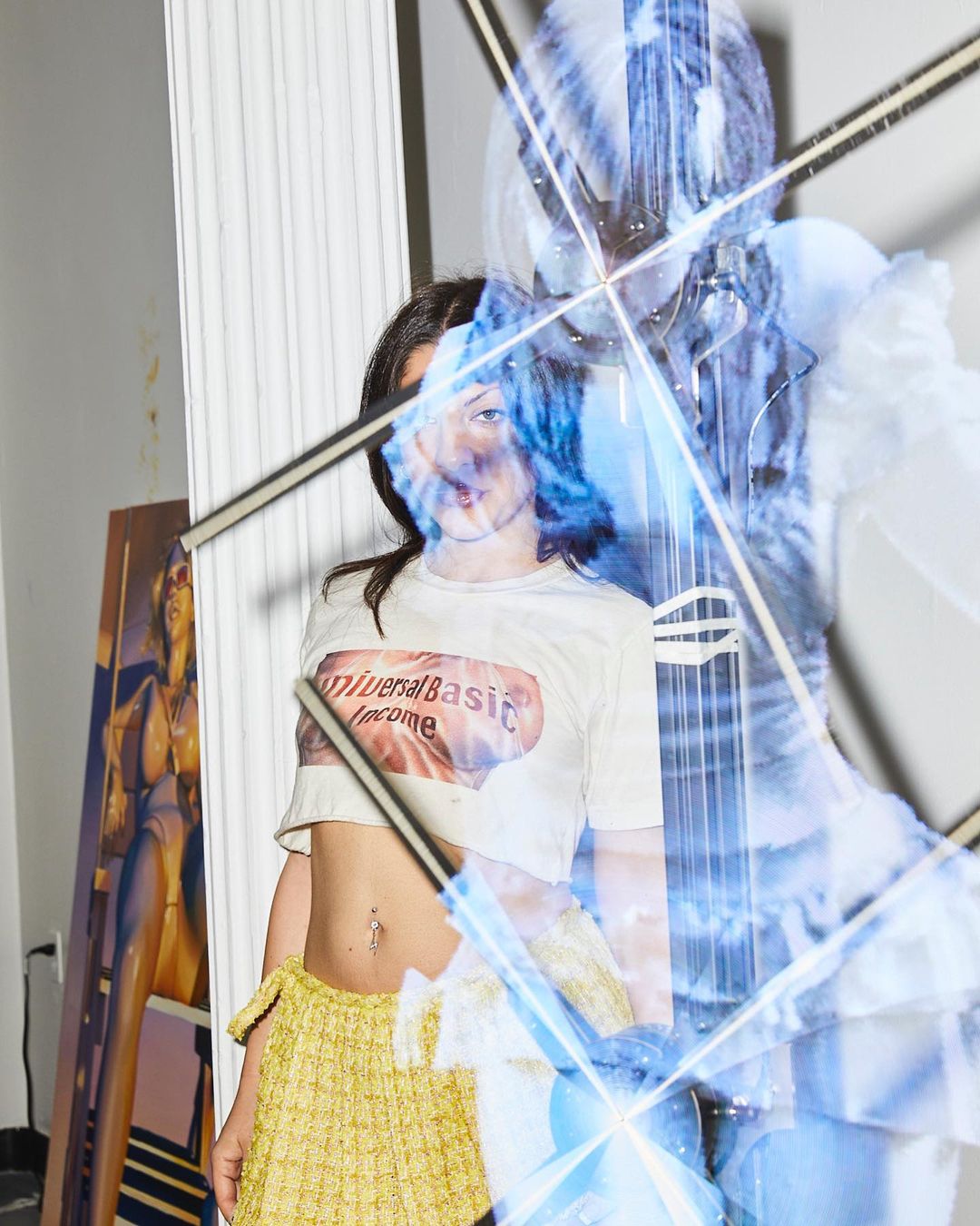 Young woman in crop top and yellow skirt with art and light effects in photo studio. Indoor shot features contemporary fashion.