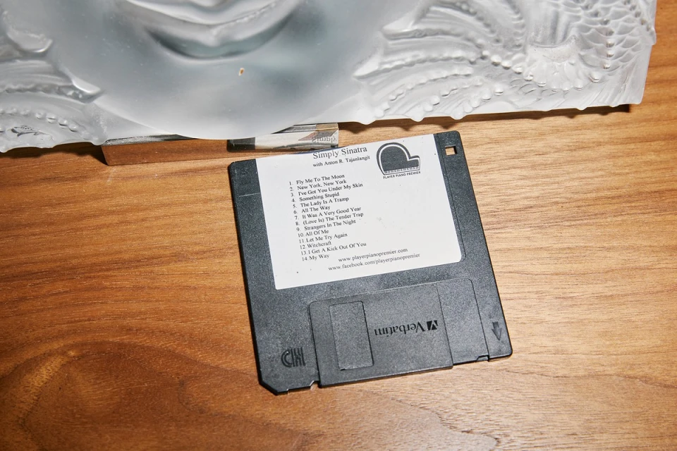 Floppy disk featuring album art for Simply Sinatra with Anton B. Tajanlangh, placed on a wooden surface next to an abstract sculpture.