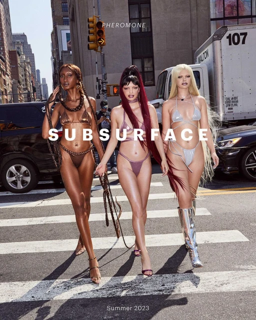 Three women in bikinis cross a city street on a sunny day, with cars and buildings in the background and the text 'Subsurface Summer 2023'.