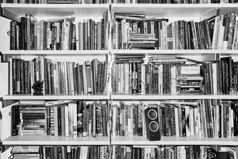 Black and white bookcase shot. Books of various sizes and colors fill the shelves, with a speaker on the bottom shelf.
