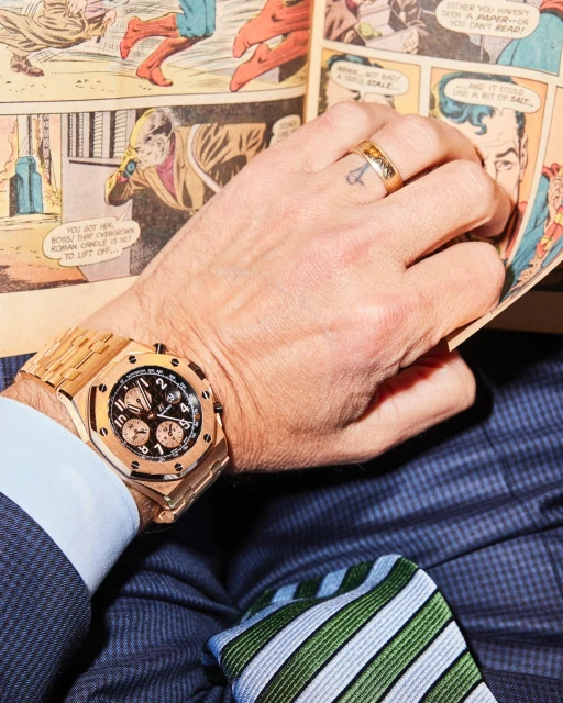 Adult male in suit reads comic book with gold watch and ring. Close-up, indoor shot.