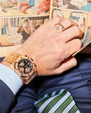 Adult male in suit reads comic book with gold watch and ring. Close-up, indoor shot.