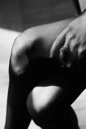 Monochrome close-up of a person wearing sheer tights with a detailed ring on their finger near the knee.