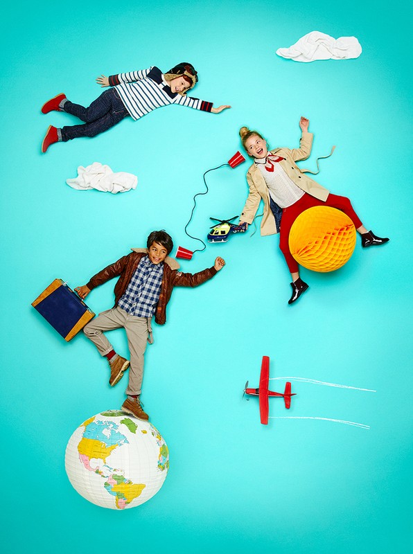 Three children in travel-themed studio photography: a boy standing on a globe with a suitcase, a girl on a honeycomb ball, and a boy flying.