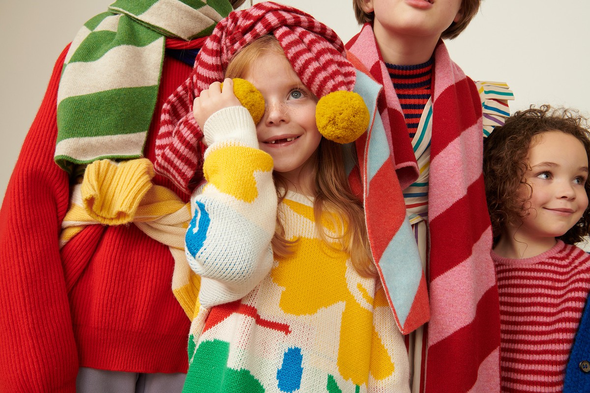 Group of children wearing colourful knitwear and accessories. Child in foreground wearing a white sweater with yellow and blue detail.