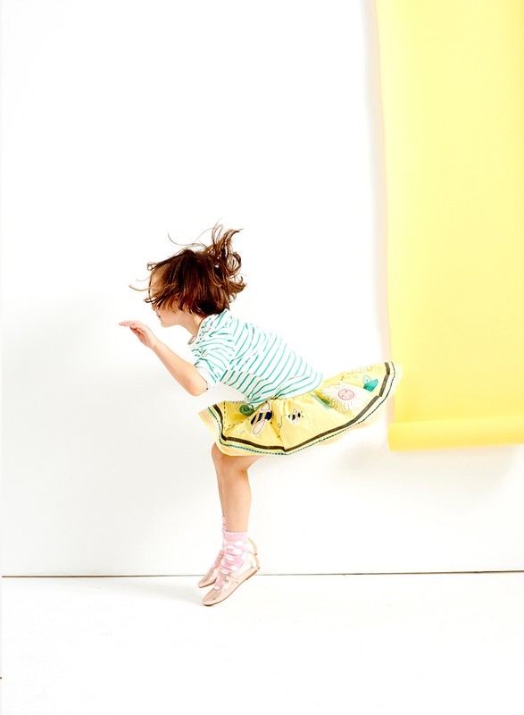 A young child in a striped shirt and yellow skirt is jumping in the air against a white backdrop with a yellow paper roll.