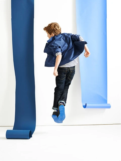 Young boy in mid-air jump wearing a denim jacket and jeans, photographed in a studio with blue paper rolls in the background.