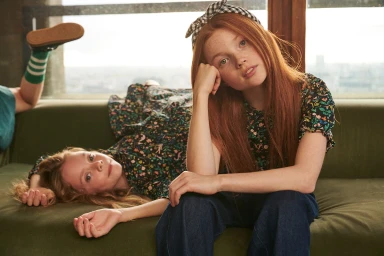 Two young red-haired girls lounging on a green sofa, photographed by Joanna Paterson.