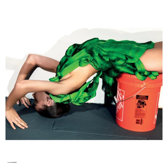 Fashion shot of a woman in a green dress arching her back, with her head near the floor and the dress draped on an orange bucket.