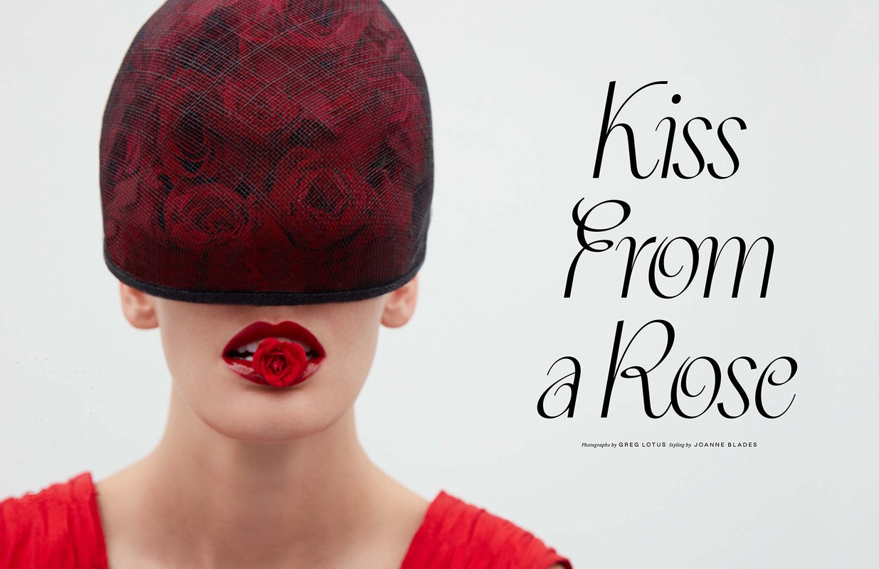Close-up fashion shot of a woman with a red rose in her mouth and a rose-patterned cap obscuring her eyes against a bright background.