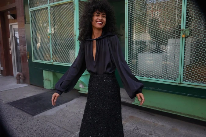 Smiling woman with dark curly hair wearing a dark silk blouse and textured skirt on a city sidewalk in Los Angeles