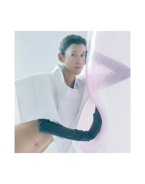 Avant-garde fashion shot: Asian woman poses in a white sculptural top and black gloves, against a gradient light pink and white backdrop.