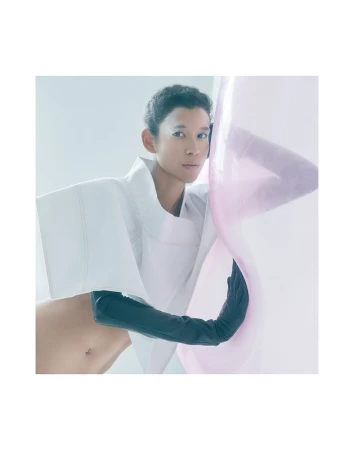 Avant-garde fashion shot: Asian woman poses in a white sculptural top and black gloves, against a gradient light pink and white backdrop.