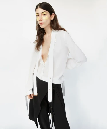 Brunette woman in a white top and black skirt poses against a white background, showcasing makeup and fashion in a studio setting.