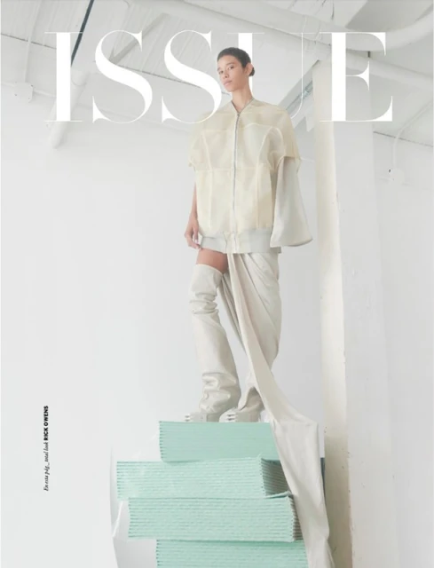Fashion editorial shot of a person in cream-colored apparel posing on a teal structure in an all-white indoor photo studio.