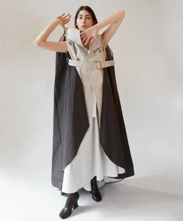 Model wearing a structured layered trench coat dress and dark shoes posing against a white background.