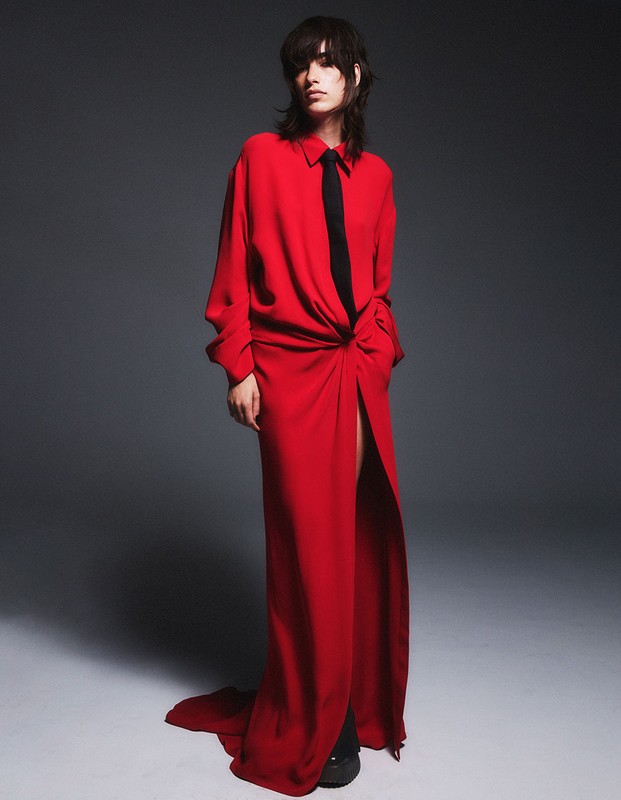 Model in a long red dress with a black tie standing against a grey backdrop styled by Joanne Blades.