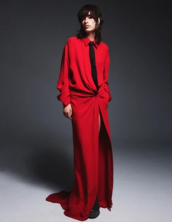 Model in a long red dress with a black tie standing against a grey backdrop styled by Joanne Blades.