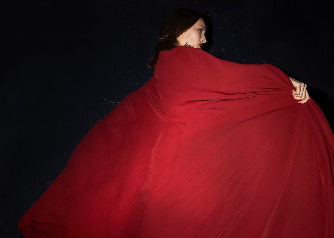Side view of a woman in a flowing red gown against a dark background, showcasing movement and fabric texture.